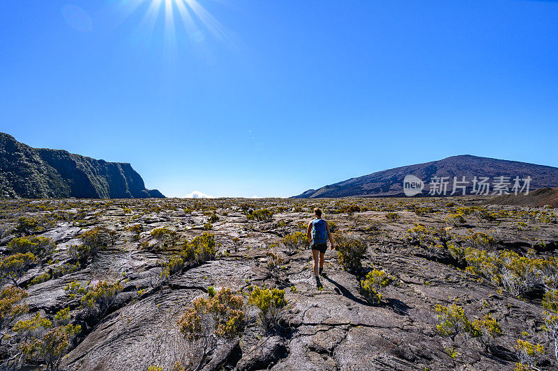 一名女游客在山顶下现存火山口凝固的熔岩场中间的小火山口附近走过自然火山景观。Formica Leo, Piton de la Fournaise，留尼旺岛，法国，欧洲。